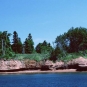 Photographie couleur de l’eau, du rivage rocailleux rouge et d’arbres