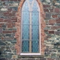 Colour photograph of gray, red and black stone wall and arched, multi-paned church window