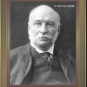 Black and white image of bald man with white hair and mustache in a suit