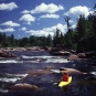 Colour photograph of person in yellow kayak, shooting rapids