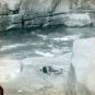 Colour image of river and rocky shoreline with man in a hole with head and feet sticking up
