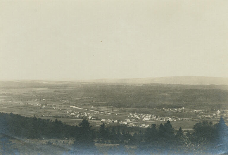 Black and white photograph of town in distance, fields and trees