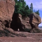 Colour photograph of red rock cliffs and tall formations with person standing on beach
