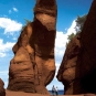 Colour photograph of tall, red rock formation with two people on beach
