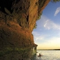 Colour photograph of a red rock cliff on the ocean with person in a kayak